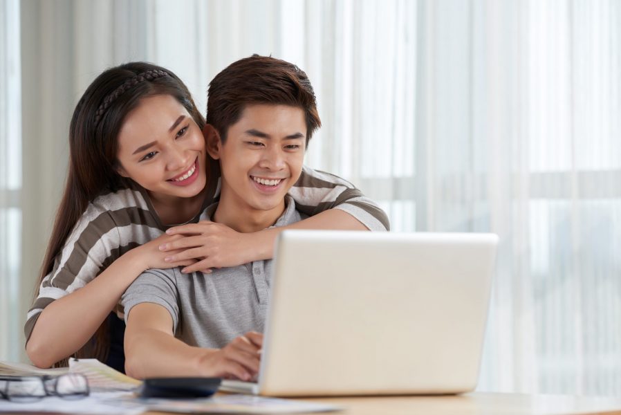 Loving Asian couple spending weekend at home: they gathered together at living room and watching favorite TV series with help of laptop